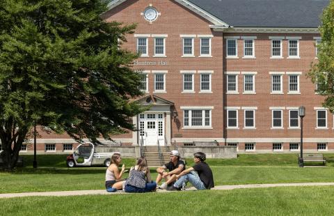 Students sitting and talking on pathway in front of brick building.